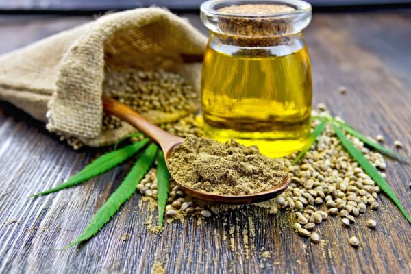 Flour hemp in a wooden spoon, hemp seed in a bag and on the table, hemp oil in a glass jar, hemp leaves on the background of wooden boards